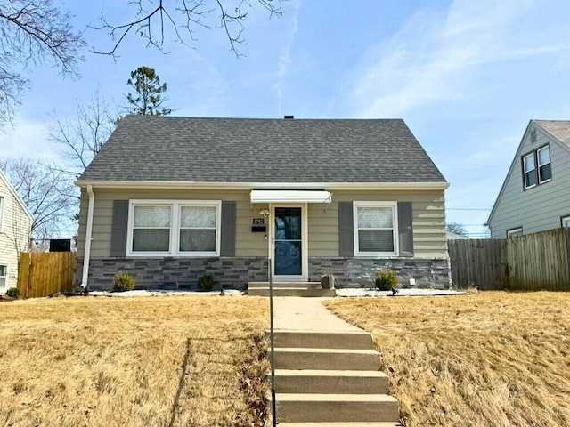 view of front of home with stone siding, a shingled roof, and fence