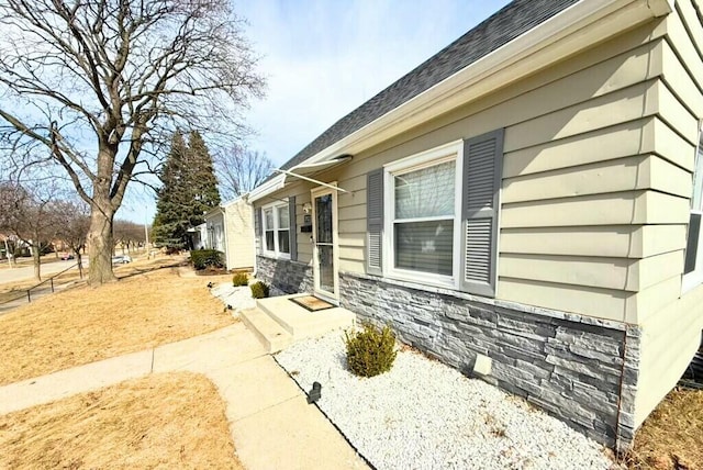 view of side of property with stone siding and roof with shingles