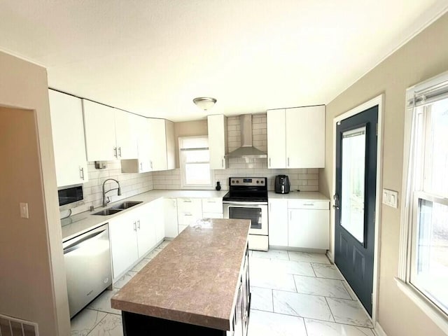 kitchen with a sink, marble finish floor, appliances with stainless steel finishes, wall chimney range hood, and tasteful backsplash