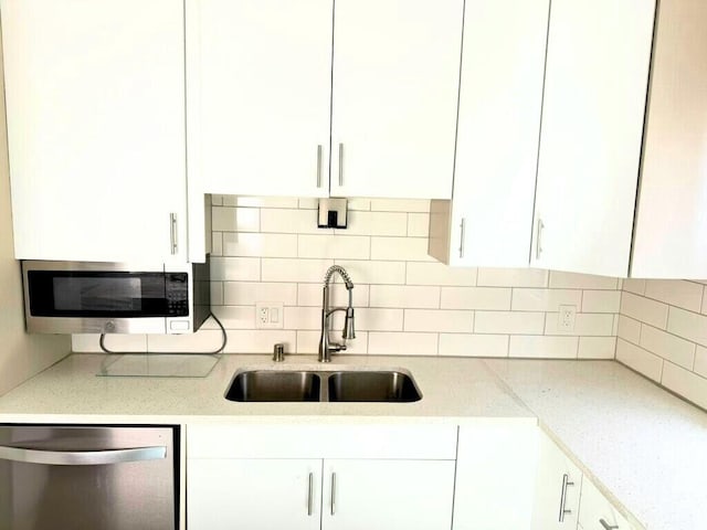 kitchen featuring backsplash, light stone counters, appliances with stainless steel finishes, white cabinets, and a sink