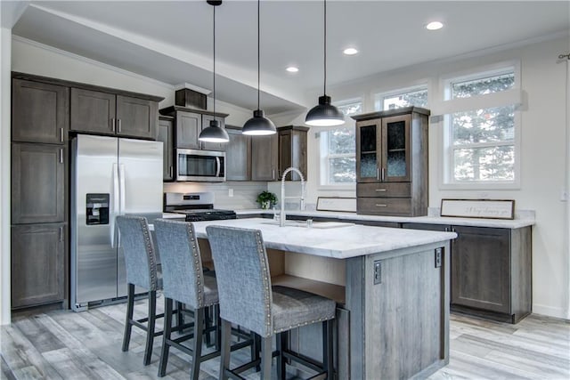 kitchen with ornamental molding, a center island with sink, light stone counters, a kitchen breakfast bar, and stainless steel appliances