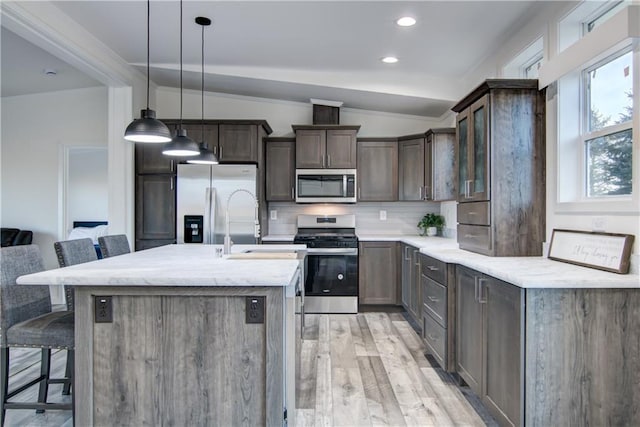 kitchen featuring dark brown cabinets, a breakfast bar, vaulted ceiling, decorative backsplash, and stainless steel appliances