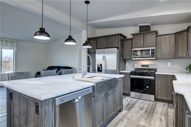 kitchen featuring light wood-type flooring, a center island with sink, stainless steel appliances, dark brown cabinetry, and decorative backsplash