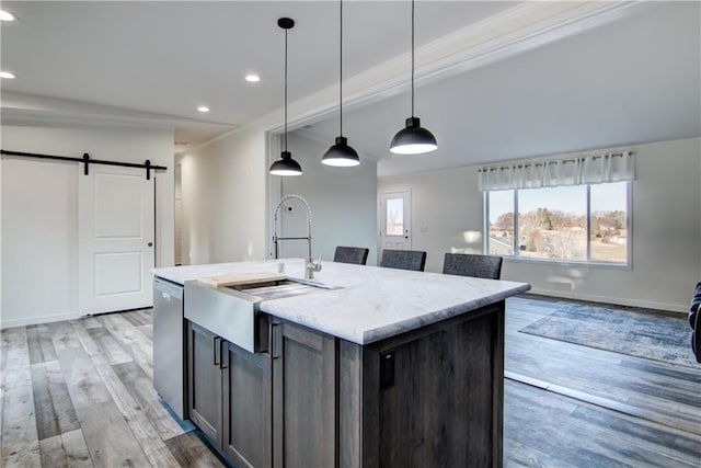 kitchen featuring light wood-style flooring, a sink, stainless steel dishwasher, a barn door, and hanging light fixtures