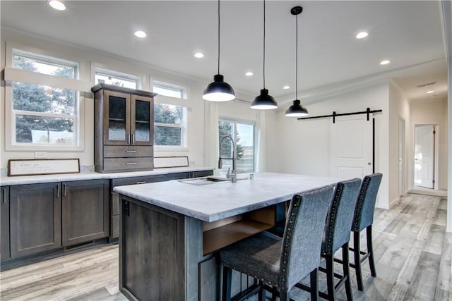 kitchen with a kitchen bar, light wood-style flooring, a barn door, crown molding, and glass insert cabinets