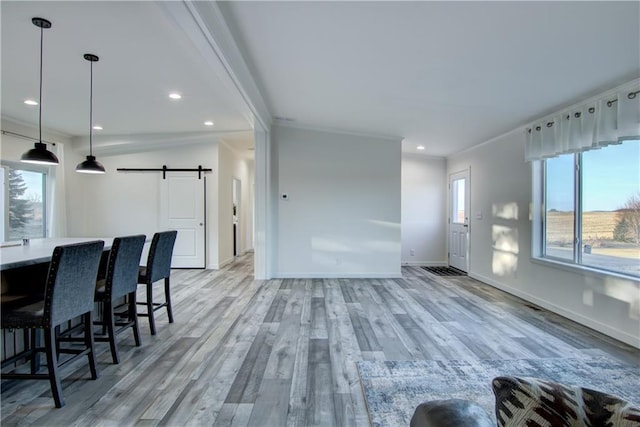 living area featuring light wood finished floors, crown molding, baseboards, a barn door, and recessed lighting