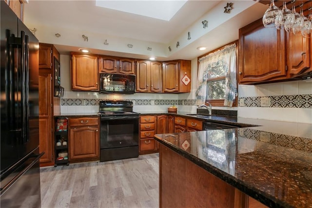 kitchen featuring brown cabinetry, dark stone countertops, and black appliances