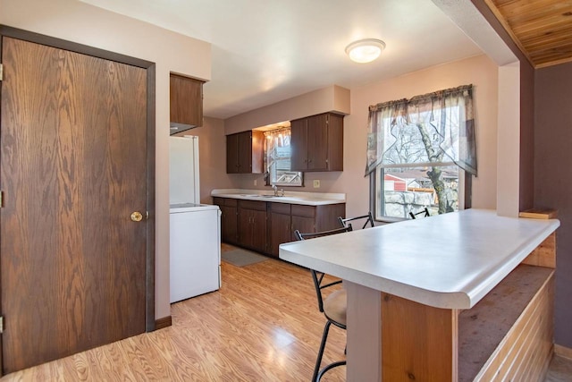 kitchen with a breakfast bar area, light countertops, washer / dryer, freestanding refrigerator, and light wood-style floors