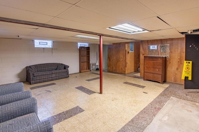 below grade area with tile patterned floors, wood walls, concrete block wall, and a paneled ceiling