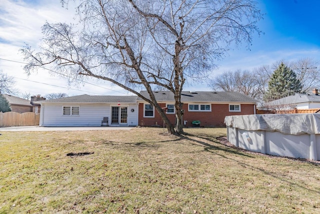 back of property featuring brick siding, a covered pool, fence, a yard, and a patio area