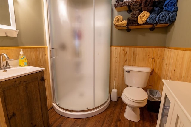 bathroom with vanity, wood finished floors, a wainscoted wall, a shower stall, and toilet