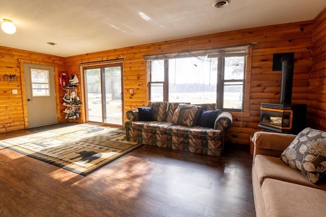 living area with a wood stove, plenty of natural light, wood finished floors, and log walls