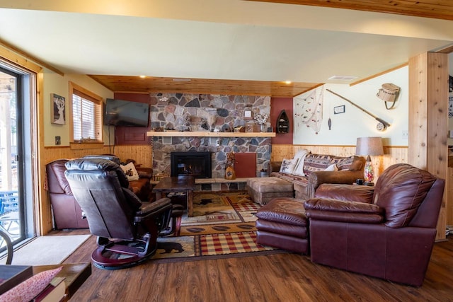 living area featuring visible vents, wooden walls, a wainscoted wall, a stone fireplace, and wood finished floors