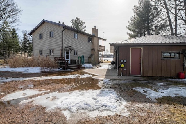 snow covered property featuring board and batten siding, a chimney, and metal roof