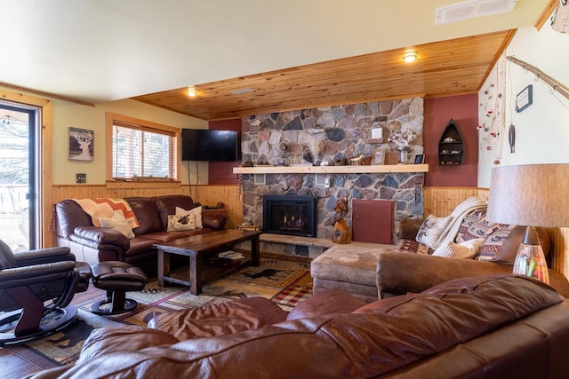 living area featuring a wainscoted wall, a stone fireplace, and wooden ceiling