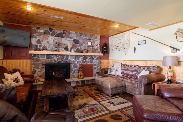 living room featuring a stone fireplace, wooden walls, wood ceiling, and wainscoting