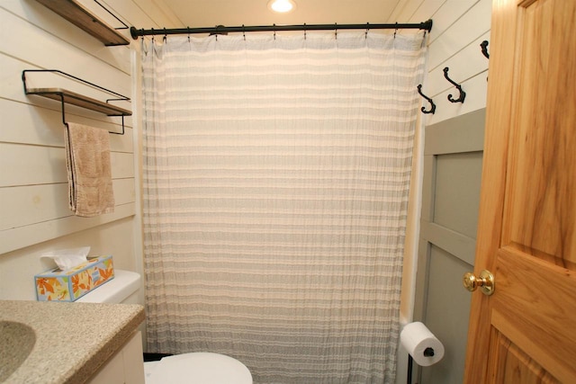 full bathroom with a shower with shower curtain, wood walls, toilet, and vanity