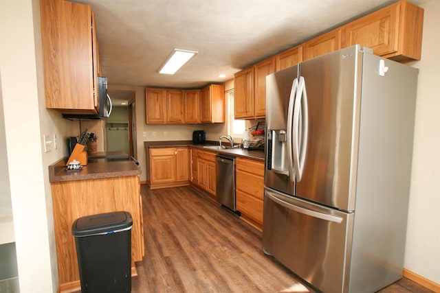 kitchen with dark countertops, baseboards, appliances with stainless steel finishes, wood finished floors, and a sink