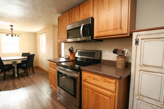 kitchen with baseboards, stainless steel appliances, dark wood-type flooring, dark countertops, and a notable chandelier