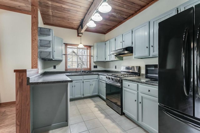 kitchen featuring under cabinet range hood, stainless steel gas stove, dark countertops, and freestanding refrigerator