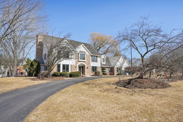 view of front facade with aphalt driveway, brick siding, a front lawn, and a playground