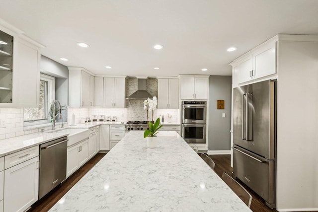 kitchen featuring white cabinetry, wall chimney range hood, light stone counters, and appliances with stainless steel finishes