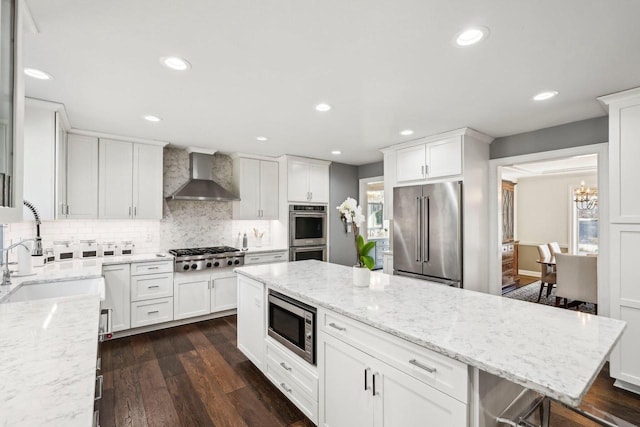 kitchen with dark wood-type flooring, a sink, stainless steel appliances, wall chimney exhaust hood, and white cabinets