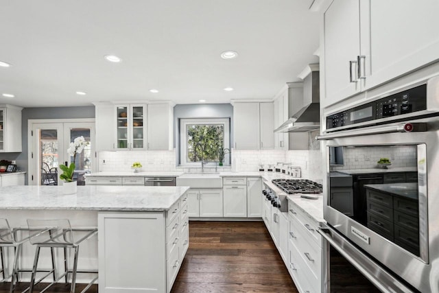 kitchen with dark wood-style floors, a sink, stainless steel appliances, white cabinets, and wall chimney exhaust hood