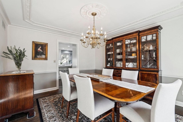 dining space featuring wood finished floors, a wainscoted wall, wallpapered walls, crown molding, and a notable chandelier