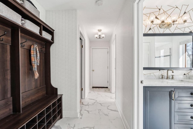 interior space featuring marble finish floor, a sink, an inviting chandelier, wallpapered walls, and baseboards