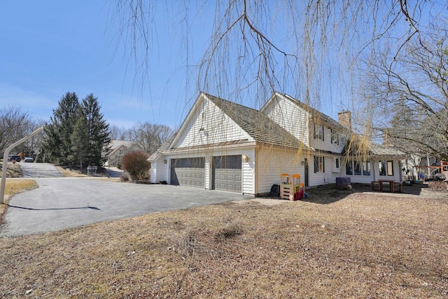 view of property exterior featuring aphalt driveway, a garage, and a chimney