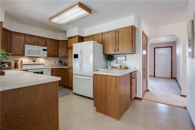 kitchen with white appliances, arched walkways, a sink, light countertops, and brown cabinets