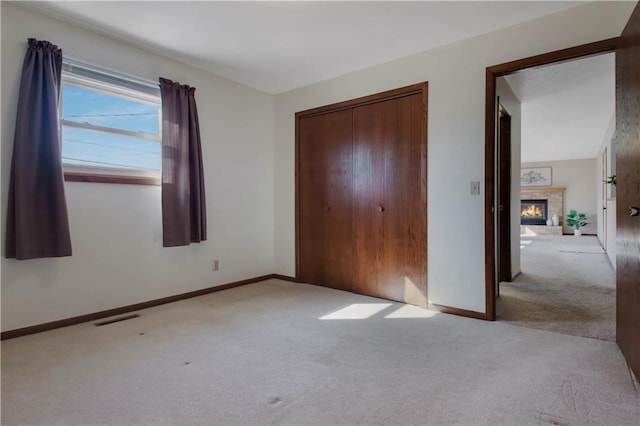 unfurnished bedroom featuring visible vents, carpet floors, baseboards, a fireplace, and a closet