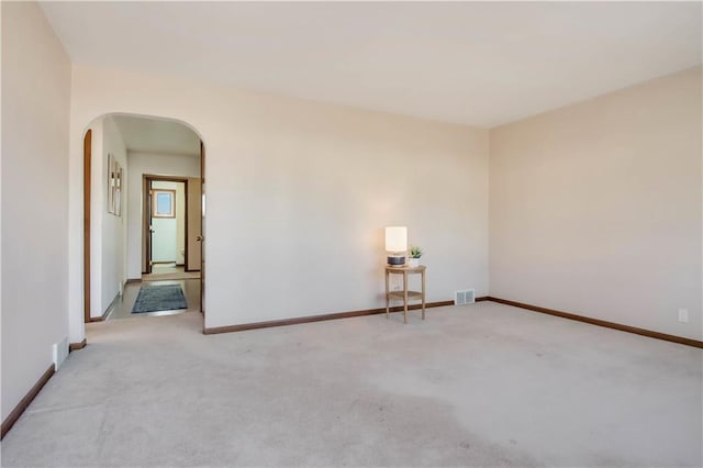 carpeted empty room with baseboards and arched walkways