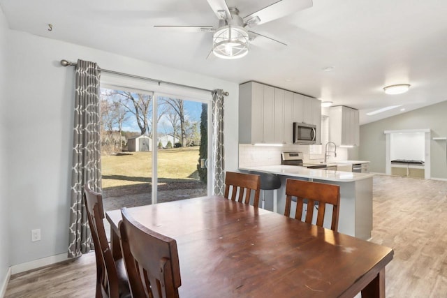 dining space with ceiling fan, light wood-type flooring, baseboards, and vaulted ceiling