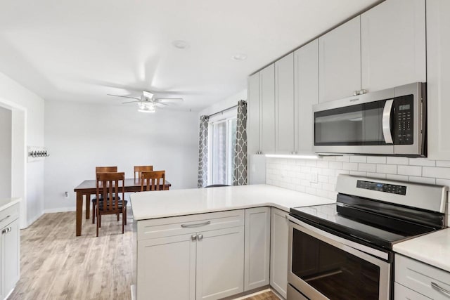 kitchen featuring light wood-style flooring, stainless steel appliances, a peninsula, light countertops, and decorative backsplash