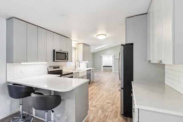 kitchen featuring light wood-type flooring, tasteful backsplash, appliances with stainless steel finishes, a breakfast bar area, and lofted ceiling