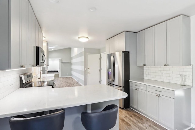 kitchen with backsplash, light countertops, a peninsula, light wood-style floors, and stainless steel appliances