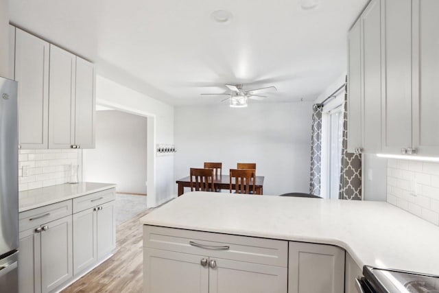 kitchen with light wood-type flooring, a ceiling fan, backsplash, a peninsula, and light countertops