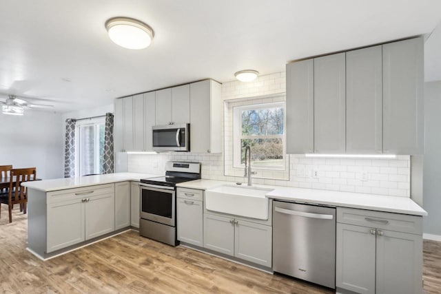 kitchen featuring gray cabinetry, light wood-type flooring, appliances with stainless steel finishes, a peninsula, and a sink