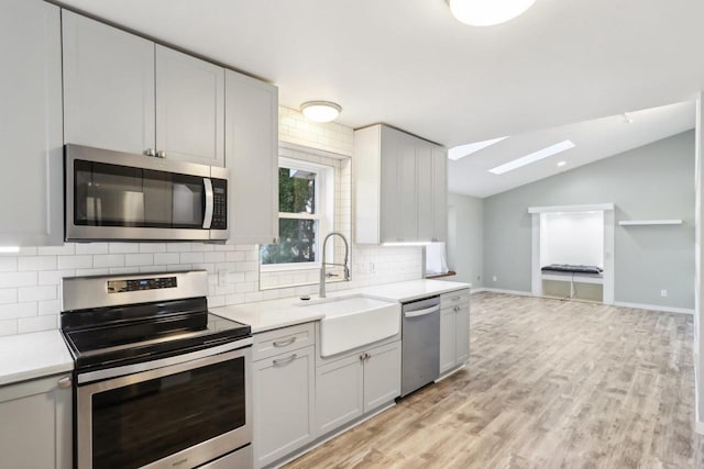 kitchen featuring a sink, backsplash, appliances with stainless steel finishes, light countertops, and vaulted ceiling