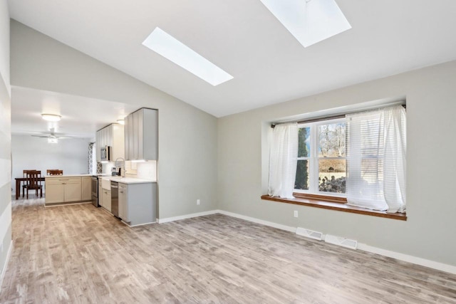 unfurnished living room with light wood finished floors, visible vents, vaulted ceiling with skylight, and baseboards