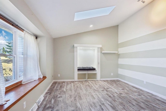 unfurnished room featuring lofted ceiling with skylight, recessed lighting, wood finished floors, and baseboards