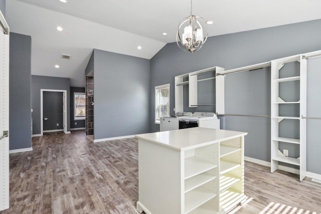 walk in closet with wood finished floors, visible vents, washing machine and clothes dryer, an inviting chandelier, and lofted ceiling