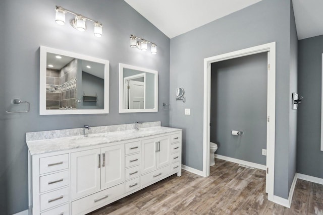 full bathroom with wood finished floors, baseboards, double vanity, a sink, and toilet