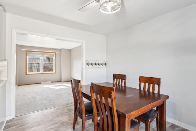 dining space featuring light colored carpet, baseboards, light wood finished floors, and ceiling fan