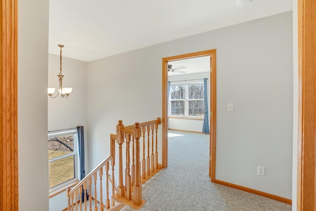 corridor featuring an upstairs landing, carpet flooring, a notable chandelier, and baseboards