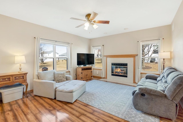 living area featuring ceiling fan, baseboards, wood finished floors, and a tiled fireplace