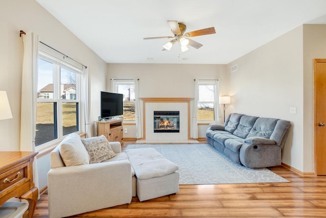 living room featuring a ceiling fan, baseboards, visible vents, light wood-style flooring, and a fireplace with flush hearth