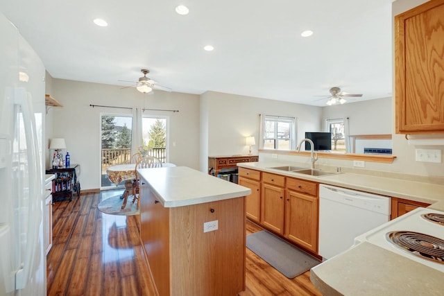 kitchen featuring a sink, a kitchen island, wood finished floors, white appliances, and light countertops